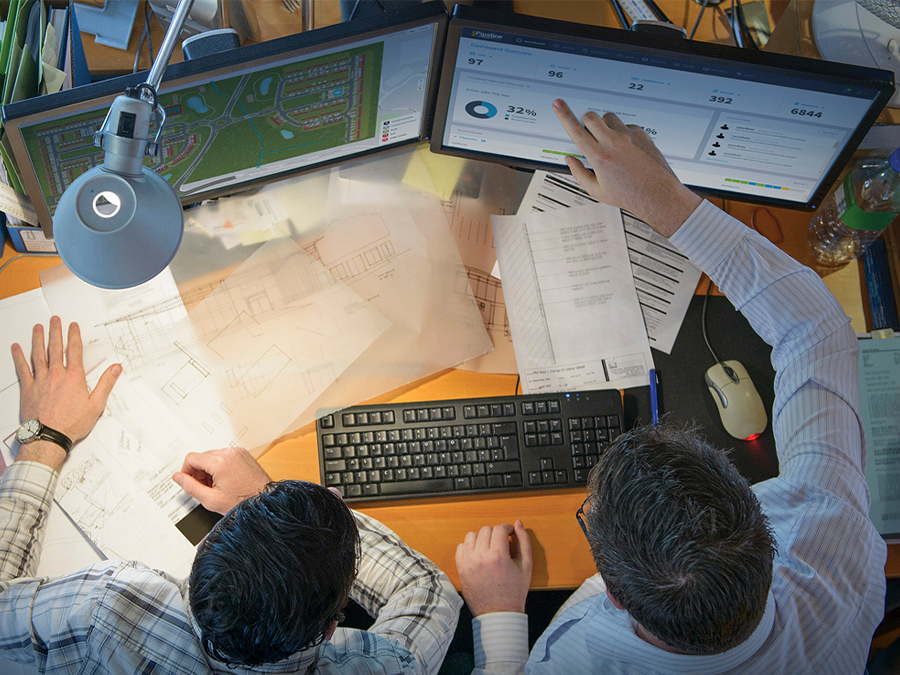 Two professionals looking at building technology software on computer screens.