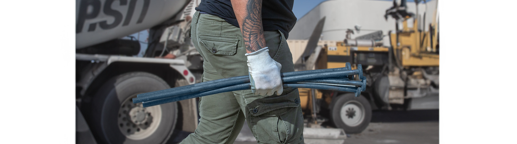 Man with white glove holding a hand full of SABR Anchor bolts on a construction site wearing green cargo pants and black tee shirt.