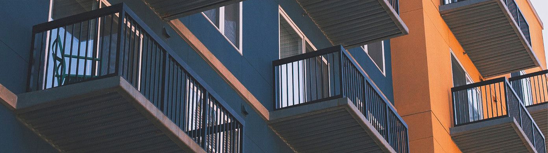 Side of blue and tan building, with balconies and windows.