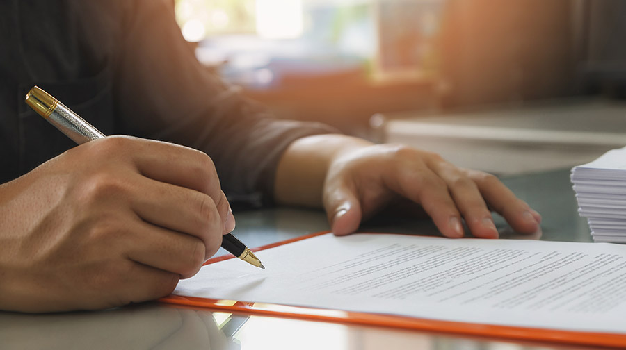 Man signing contract on a desktop.