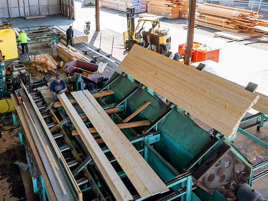 Wood manufacturing facility with workers operating machinery and processing lumber planks.