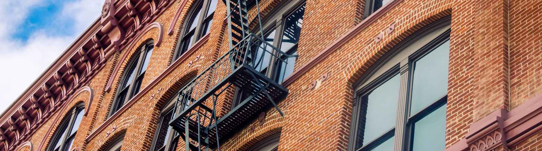Upward view side of red brick building with metal stair case and four panel windows