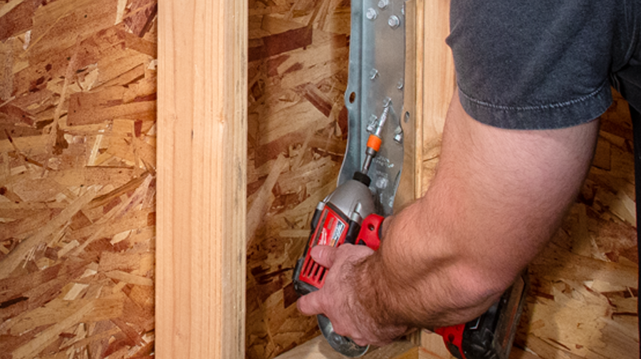 Man using red drill gun to install HDUE7 product into wooden panel.