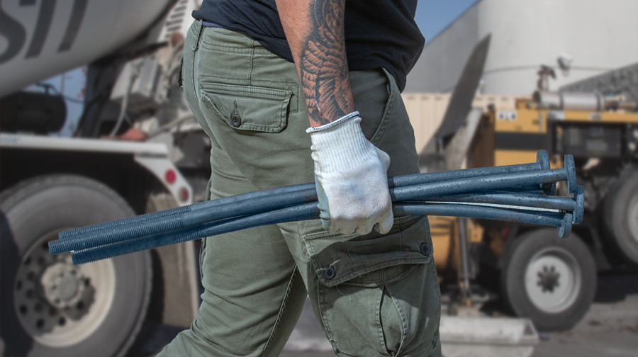 Man with white glove holding a hand full of SABR Anchor bolts on a construction site wearing green cargo pants and black tee shirt.