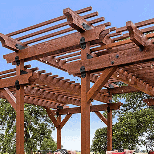 A large wooden pergola with black metal connectors, featuring slatted beams and an open-air design for outdoor dining.