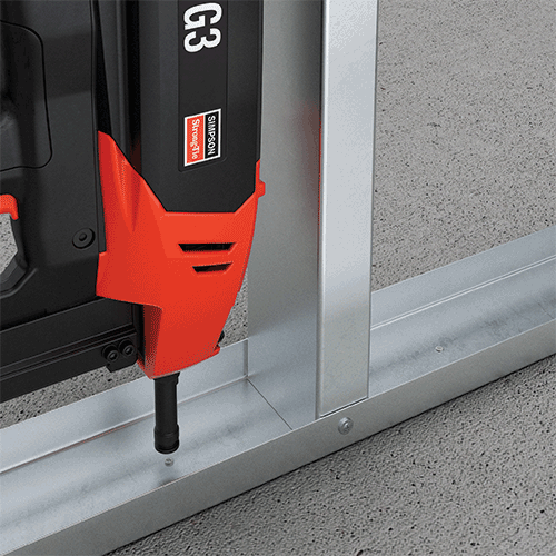 Simpson Strong-Tie G3 gas fastening tool being used to drive a pin into a metal framing track on concrete flooring.