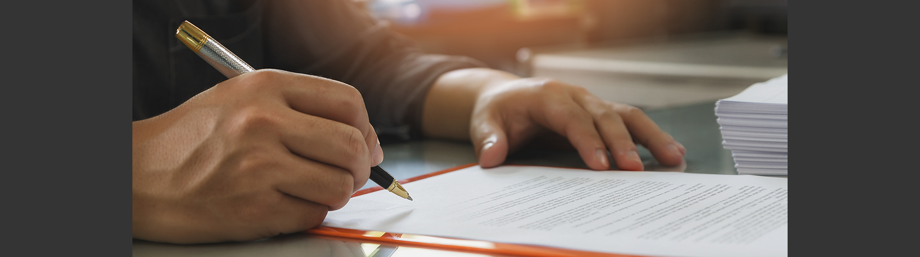 Man's hand holding a metal pen signing a contract.