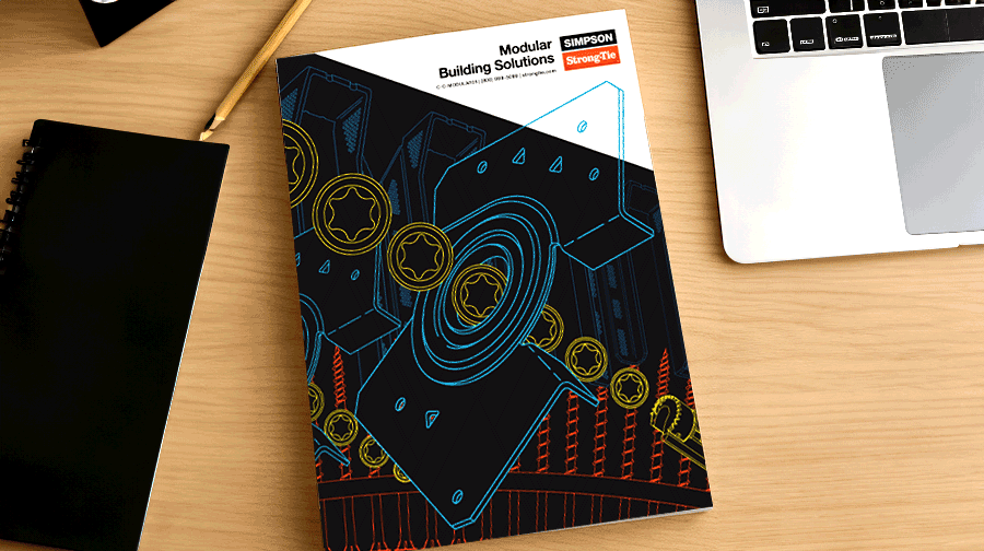 Desk with a pencil, notebook, laptop, and a booklet titled 'Modular Building Solutions' featuring abstract geometric cover art in blue, yellow, and red.