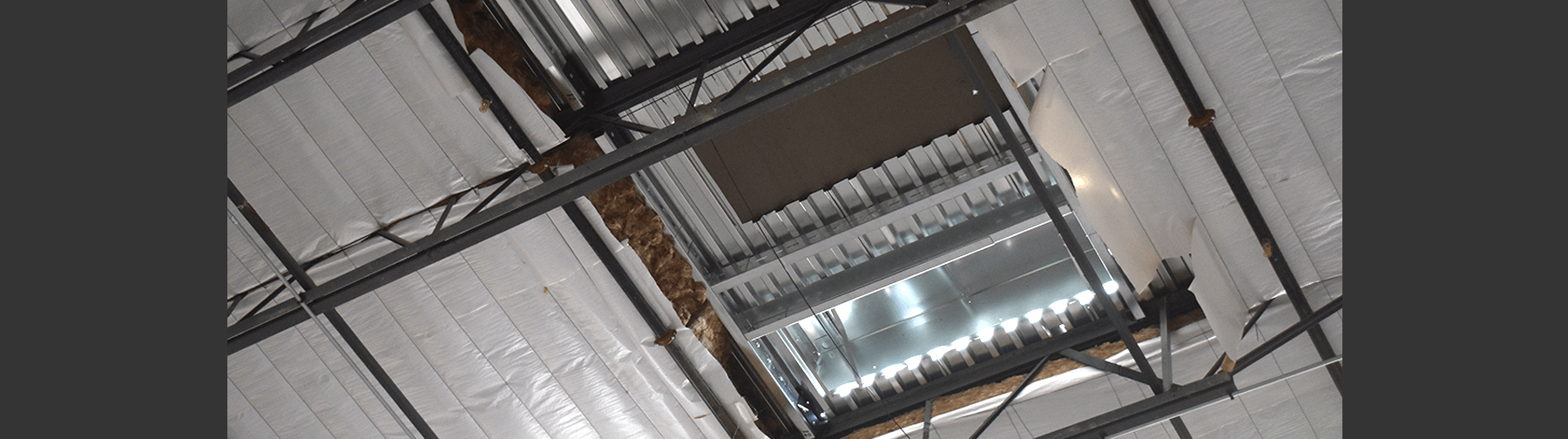 A wider view of an industrial ceiling with exposed metal framing, insulation, and a partially installed HVAC system.