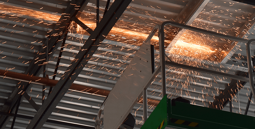 A construction worker using a cutting tool to modify a metal roof, generating bright sparks as the steel is cut.