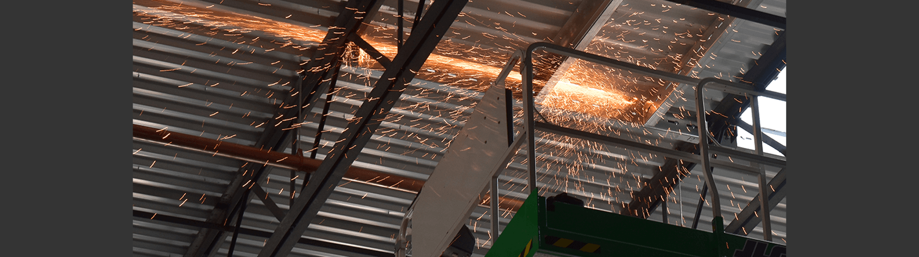 A construction worker using a cutting tool to modify a metal roof, generating bright sparks as the steel is cut.