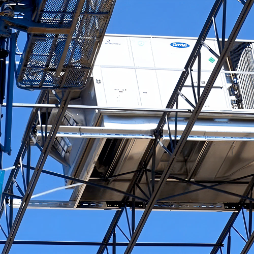 A large rooftop HVAC unit supported by a steel framing system, with a construction lift nearby under a clear blue sky.